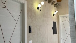A hallway with a geometric-patterned door, a wall-mounted light fixture, and a textured wall. - Santa Ciriaca - Aghìa Kyriaki (Gerace)