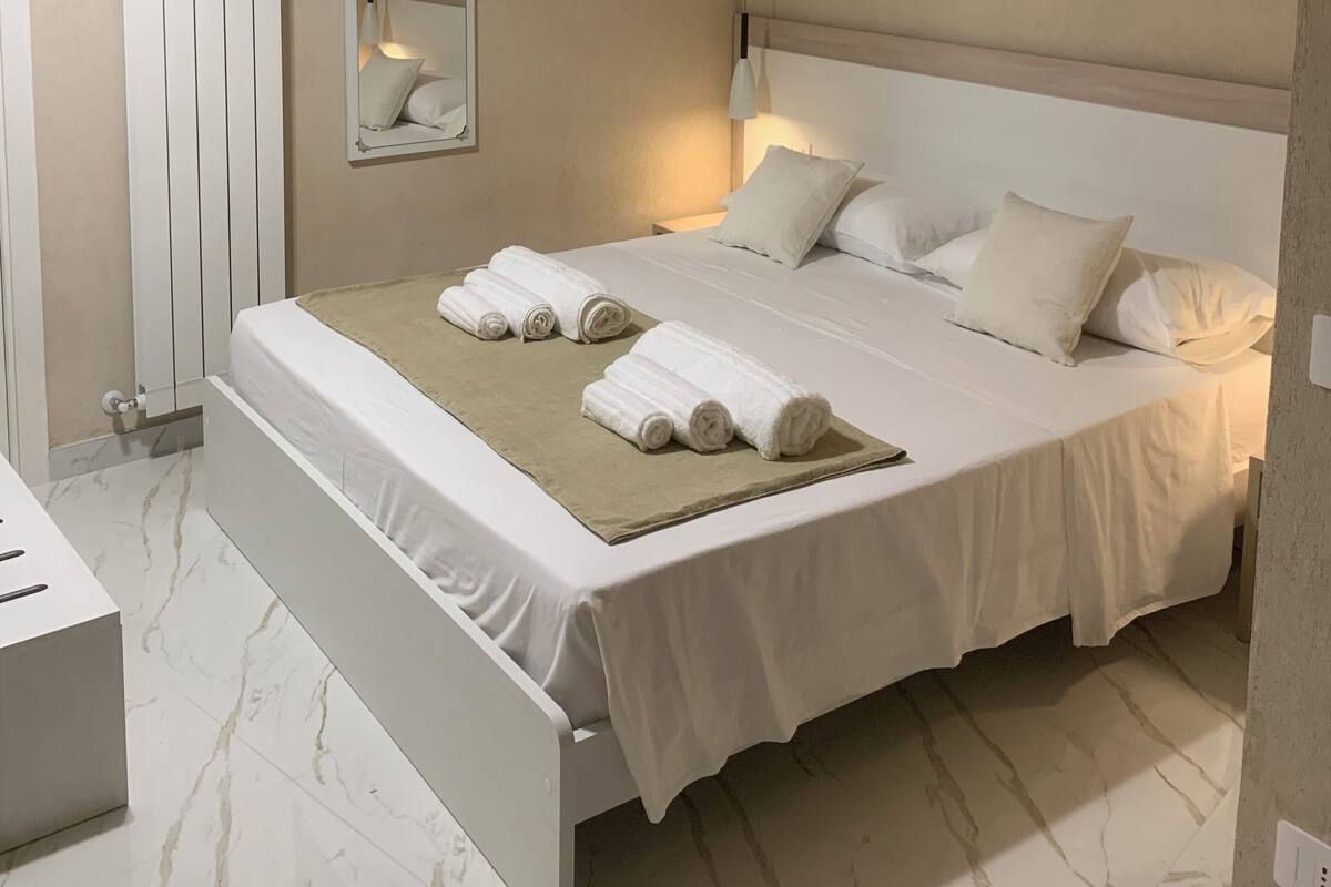 Une chambre à coucher avec un lit, des oreillers, une table de chevet, un miroir et un radiateur.