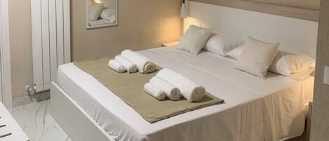 A bedroom with a bed, pillows, a bedside table, a mirror, and a radiator.