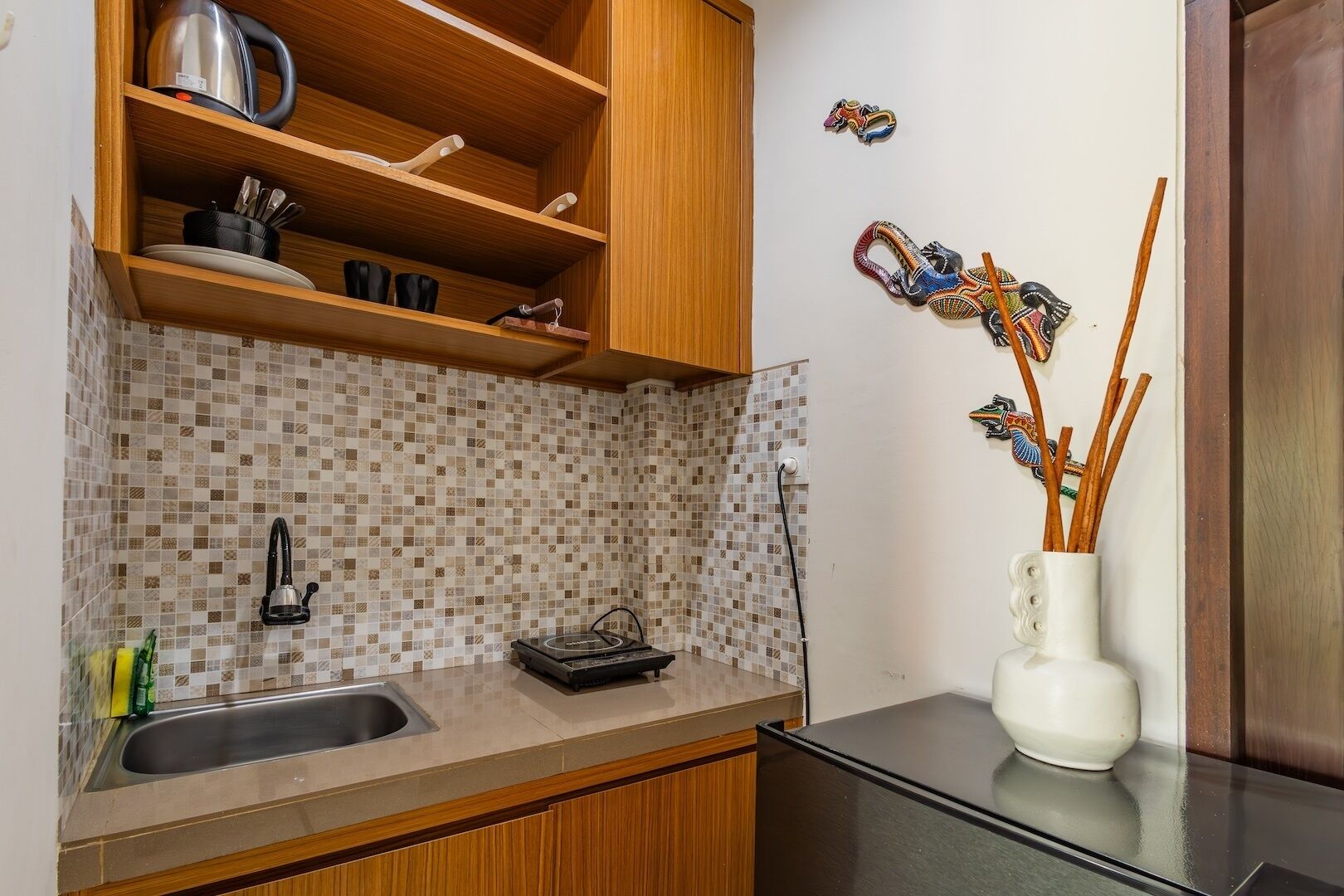 Una cucina con mobili in legno, una parete rivestita di piastrelle, un lavandino e un vaso decorativo con giunchi.