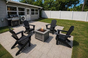 Eine Terrassengruppe im Freien mit Grill, Feuerstelle und vier Adirondack-Stühlen.