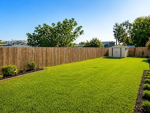Un jardin avec une clôture en bois, un abri de jardin et une pelouse bien entretenue.