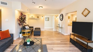 A modern living room with a sofa, coffee table, TV, and a dining area with a table and chairs.