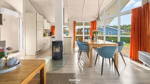 A modern kitchen with white cabinets, a black stove, and a dining area with blue chairs and a wooden table. - Möwenstübchen Ferien House in Grömitz: Sauna, A/C, 250 m to beach (Grömitz)