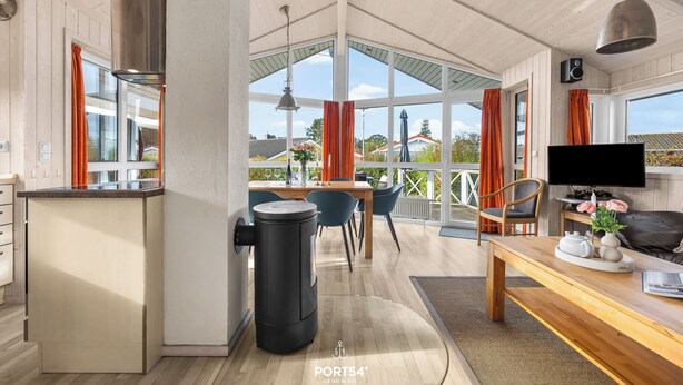 A modern kitchen with a black trash bin, wooden dining table, and a TV on a stand. - Möwenstübchen Ferien House in Grömitz: Sauna, A/C, 250 m to beach (Grömitz)