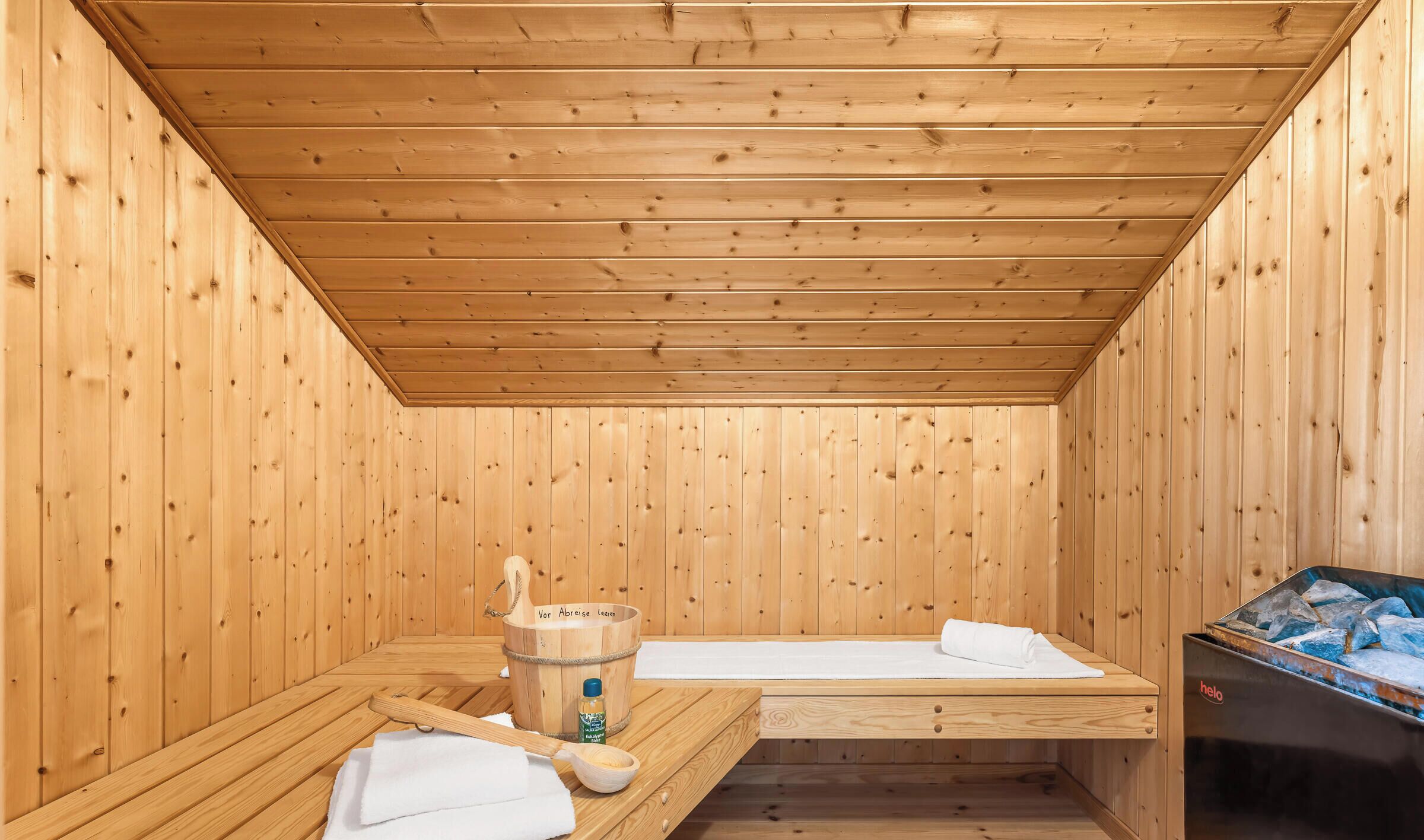A wooden sauna room with benches, a wooden bucket, and a sauna machine.