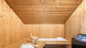 A wooden sauna room with benches, a wooden bucket, and a sauna machine.