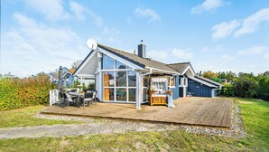 A modern house with a large glass front, a wooden deck, and a satellite dish. - Möwenstübchen Ferien House in Grömitz: Sauna, A/C, 250 m to beach (Grömitz)