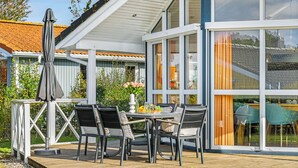 A modern outdoor patio with a table and chairs, a covered seating area, and a view of the surrounding garden and neighboring buildings.