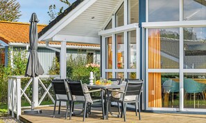A modern outdoor patio with a table and chairs, a covered seating area, and a view of the surrounding garden and neighboring buildings.