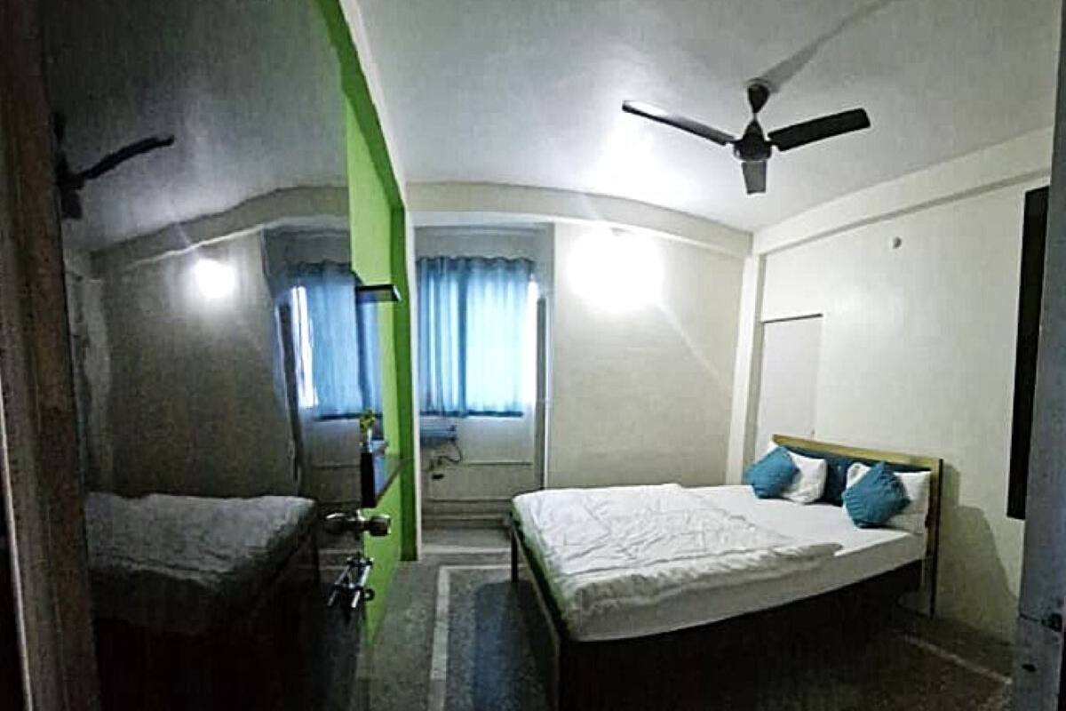 A small, compact hotel room with a single bed, a ceiling fan, and a window with curtains.