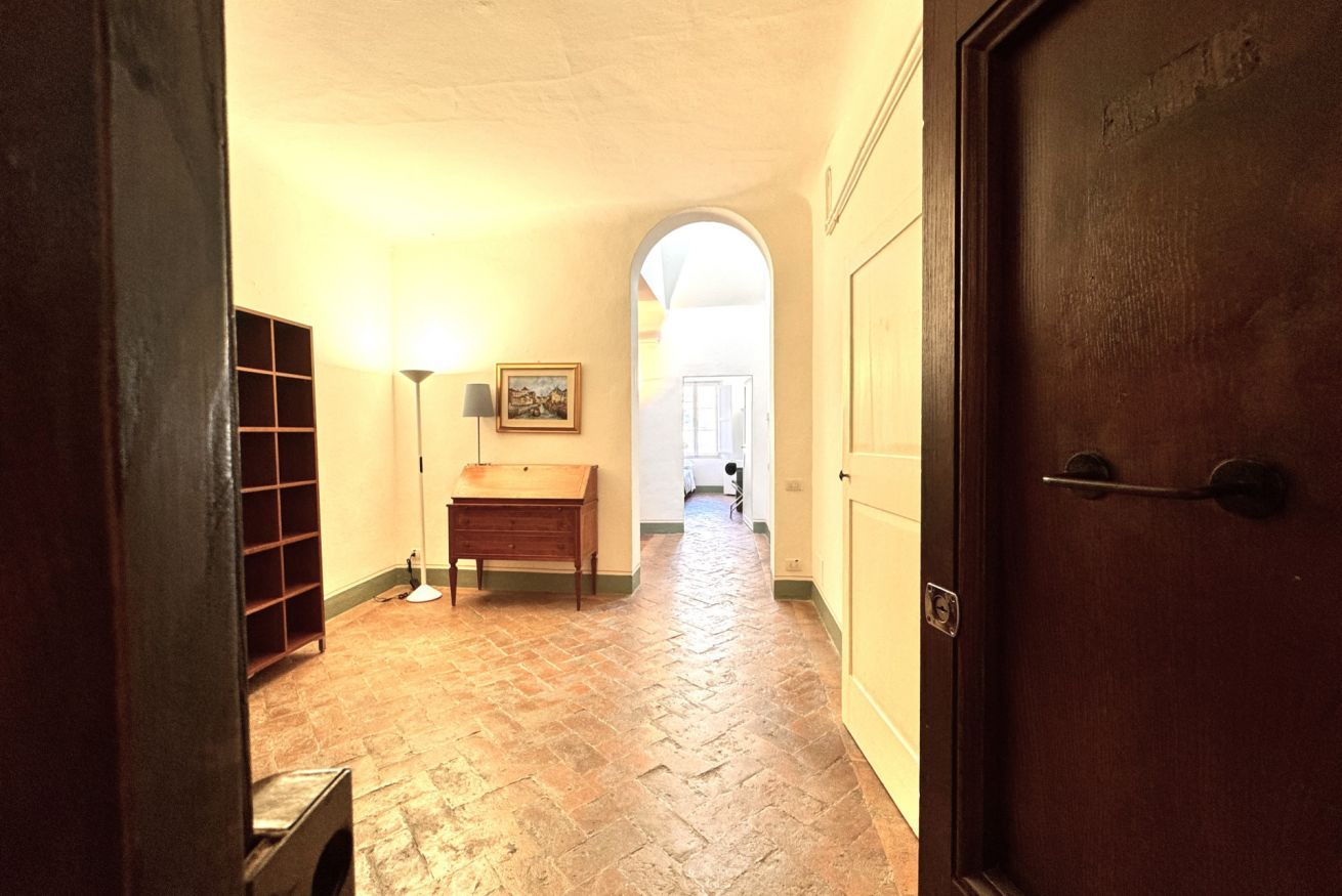 Un corridoio con pavimento in pietra, una panca di legno, una lampada e una porta.