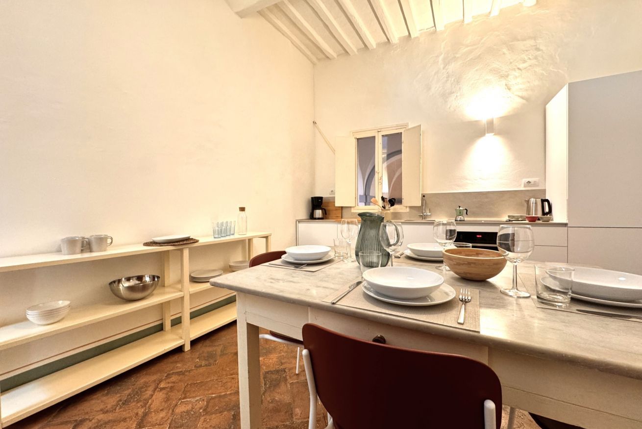 A modern kitchen with white cabinetry, a marble countertop, and a dining area with a red chair.