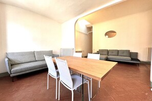 A modern living room with a wooden dining table, white chairs, a grey sofa, and a grey couch.