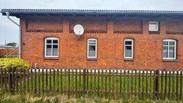 Ein Backsteinhaus mit Satellitenschüssel, drei Fenstern und einem Holzzaun.