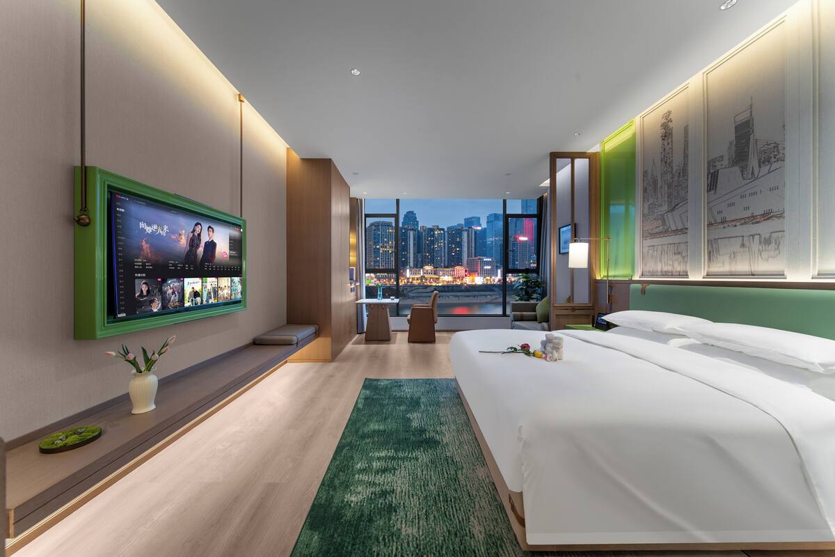 Een moderne hotelkamer met een groot bed, een aan de muur bevestigde televisie, een bureau en uitzicht op de stadshemel.