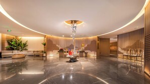 Een moderne lobby met een gepolijste marmeren vloer, een sculpturaal centraal lichtarmatuur en een zithoek met een bank en stoelen.