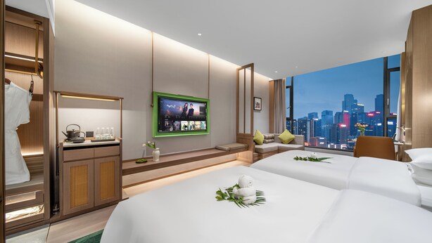 Een hotelkamer met twee bedden, een televisie, stadszicht en een houten kledingkast.