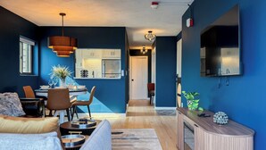 A modern living room with a sofa, coffee table, and a dining area with chairs and a table. There is a kitchen with cabinets and a refrigerator in the background. - City Views~Close 2 Salem~Balcony (Beverly)