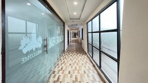 A hallway with a checkered floor, glass walls with a logo, and large windows on one side. - Hotel Nature Peak (Bardoli)