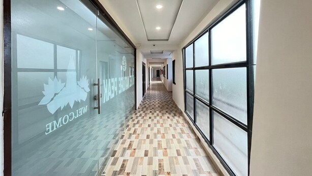 A hallway with a checkered floor, glass walls with a logo, and large windows on one side.