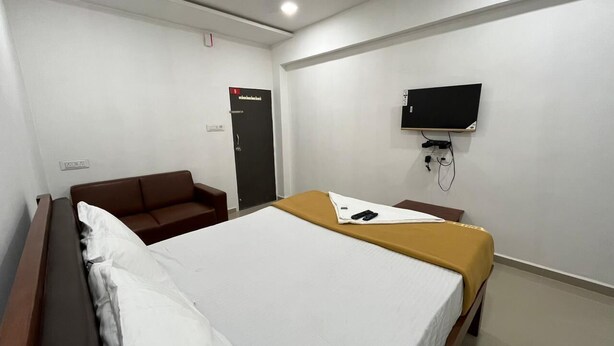 A hotel room with a single bed, a brown sofa, a television mounted on the wall, and a door with a sign. - Hotel Nature Peak (Bardoli)