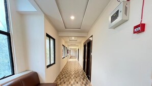 A hotel corridor with a checkered floor, a brown bench, and a fire alarm on the wall.