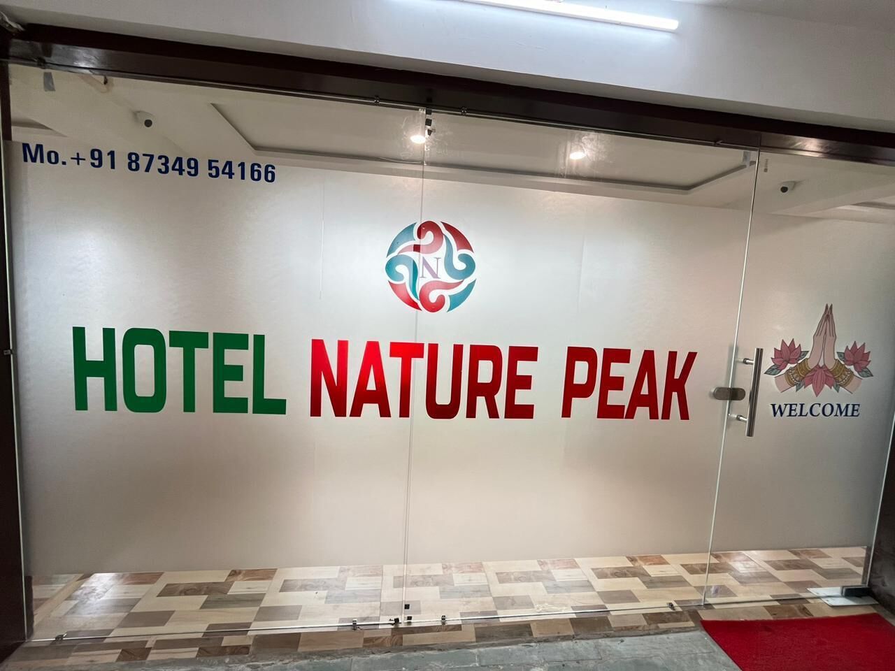 Entrada de un hotel con un número de contacto, un logotipo y el nombre 'HOTEL NATURE PEAK' bien visible.