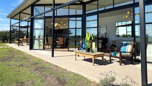 Una casa moderna con amplios ventanales, un patio con mobiliario exterior y vistas al paisaje circundante.