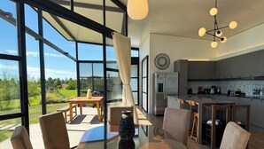 Una cocina moderna con refrigerador integrado, un comedor con mesa y sillas de vidrio, y ventanas amplias que ofrecen vistas al exterior.