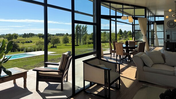 Un salón amplio con ventanas grandes, una piscina y mobiliario de exterior.