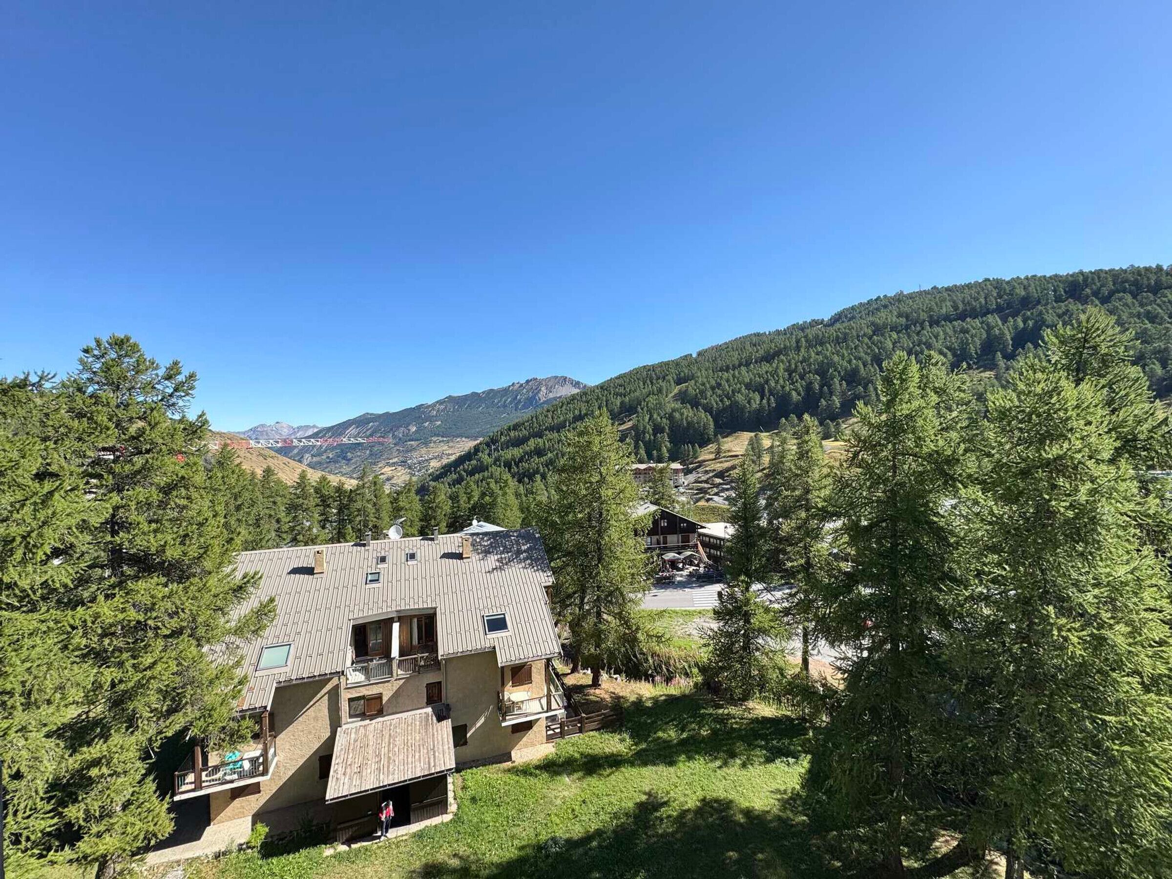 A multi-story building with a sloped roof, surrounded by dense forest and mountains in the background.