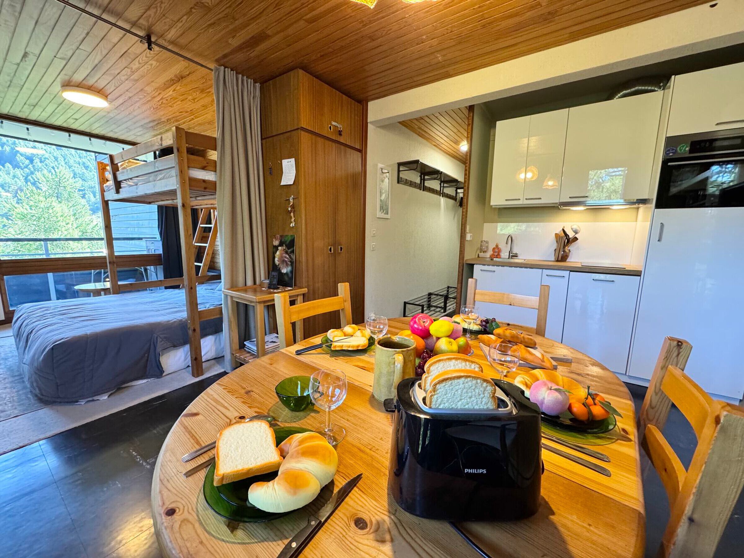 A cozy room with a bunk bed, a dining table set with bread, fruits, and a toaster.