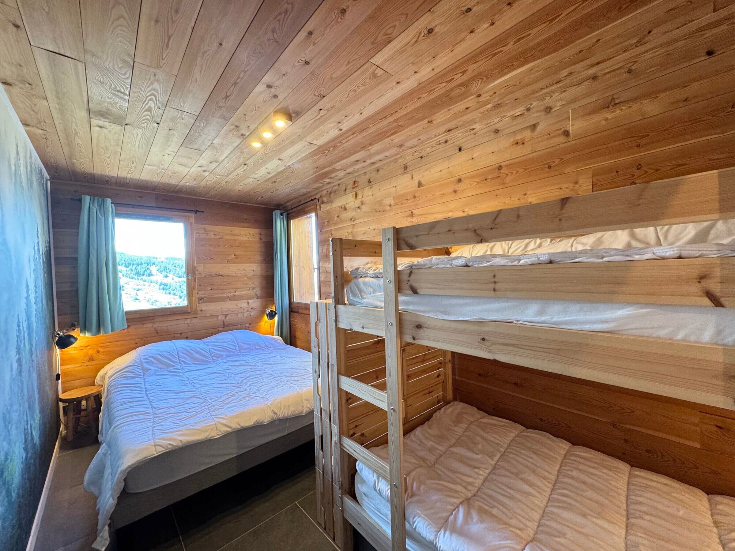 A wooden cabin room with a bunk bed, a single bed, and a window with curtains.