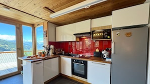 Eine moderne Küche mit weißen Schränken, einer roten Spritzschutzleiste und Blick auf die Berge durch große Fenster.