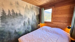 Ein Schlafzimmer mit Bett, einem Fenster mit Vorhängen und einem Wandbild von einem Wald.