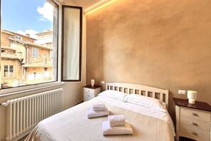 A hotel room with a bed, a window, a nightstand, and a radiator. - Casa Bruna - Via Banchi di Sotto (Siena)