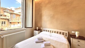 A hotel room with a bed, a window, a nightstand, and a radiator. - Casa Bruna- Via banchi di sotto (Siena)