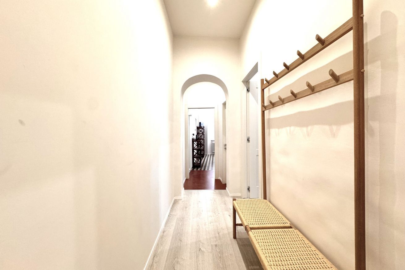 Un corridoio con una panchina di legno, un appendiabiti e una porta ad arco che conduce a un'altra stanza.