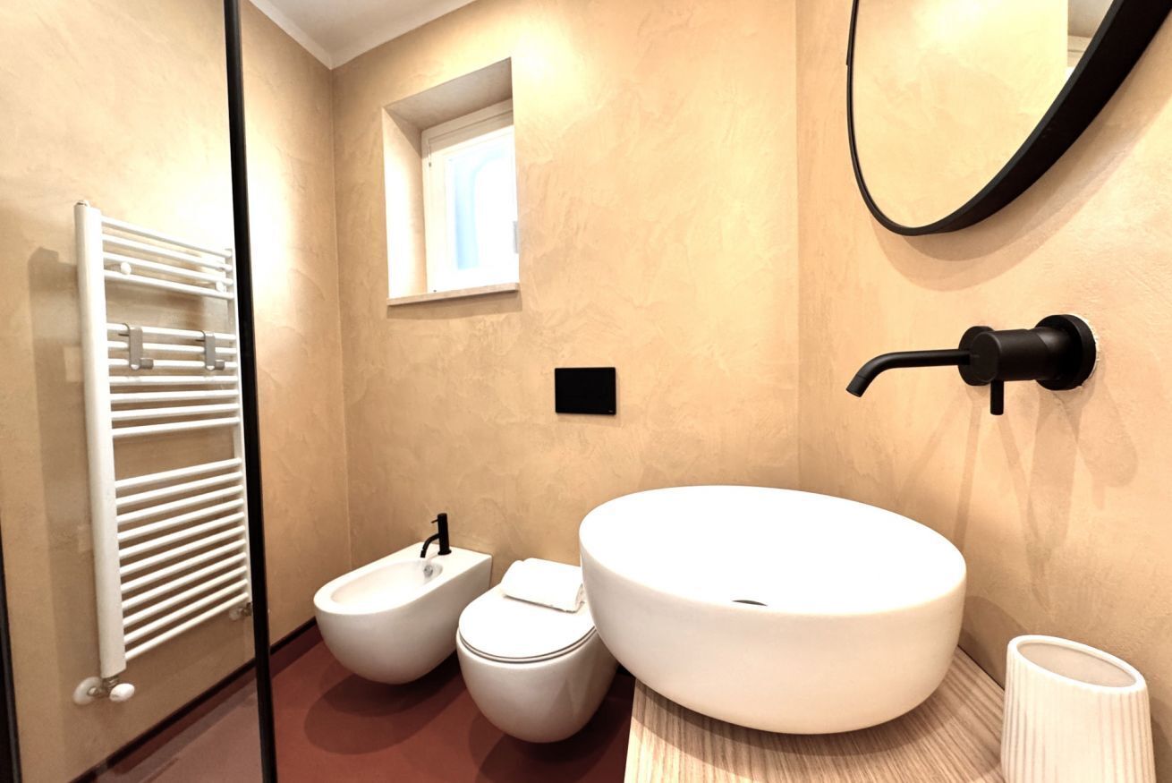 A modern bathroom with a large white sink, a bidet, and a toilet. There is a towel rack and a mirror on the wall.