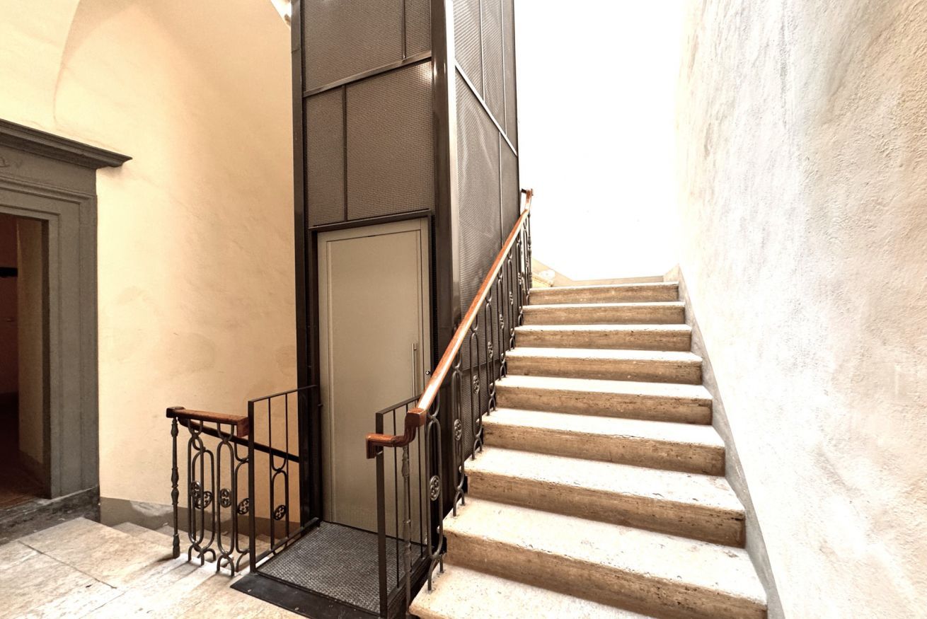 Una scala con ringhiera in legno e balaustre in metallo, che conduce a una porta provvista di inferriata.