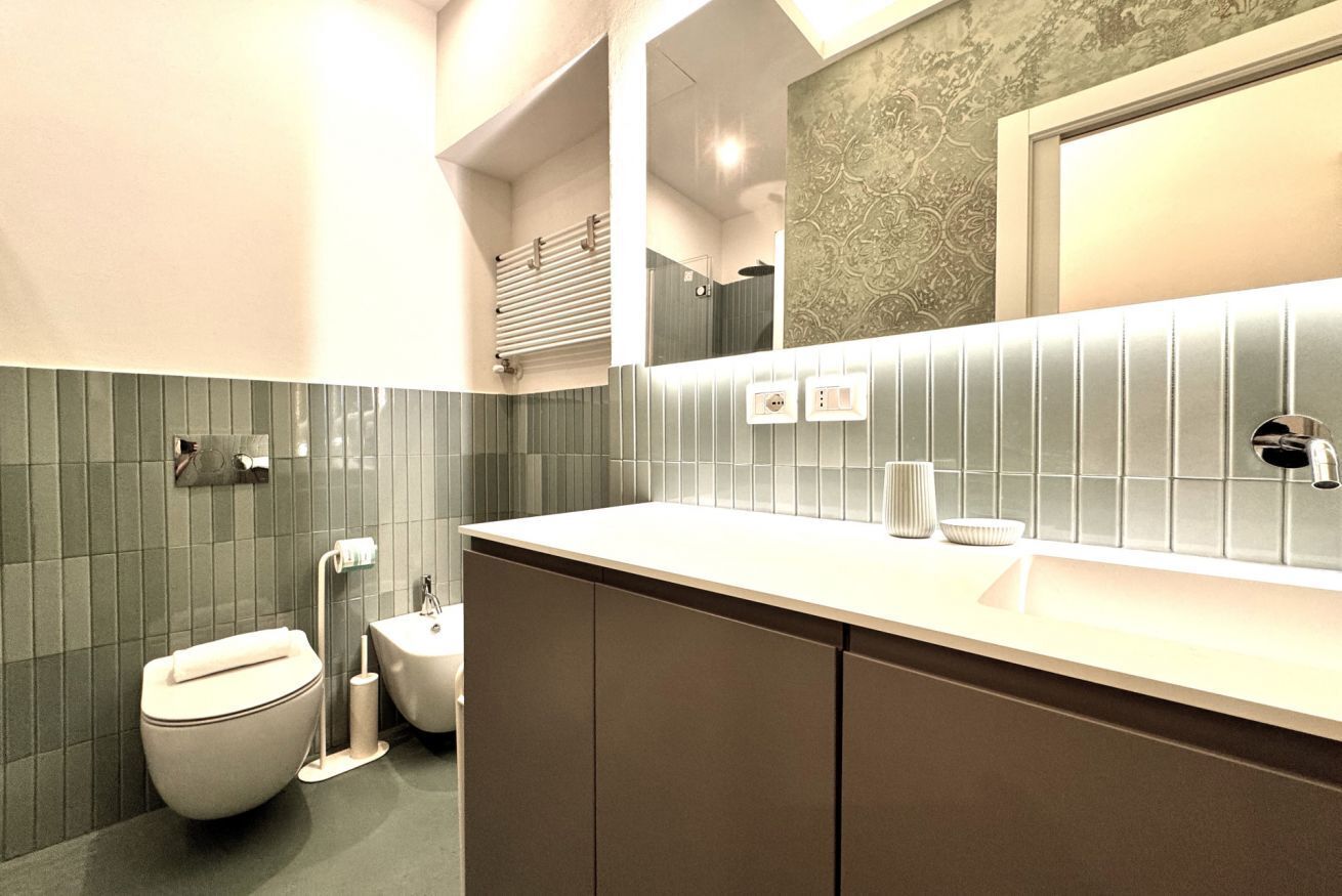 A modern bathroom with a toilet, bidet, sink, and mirror.