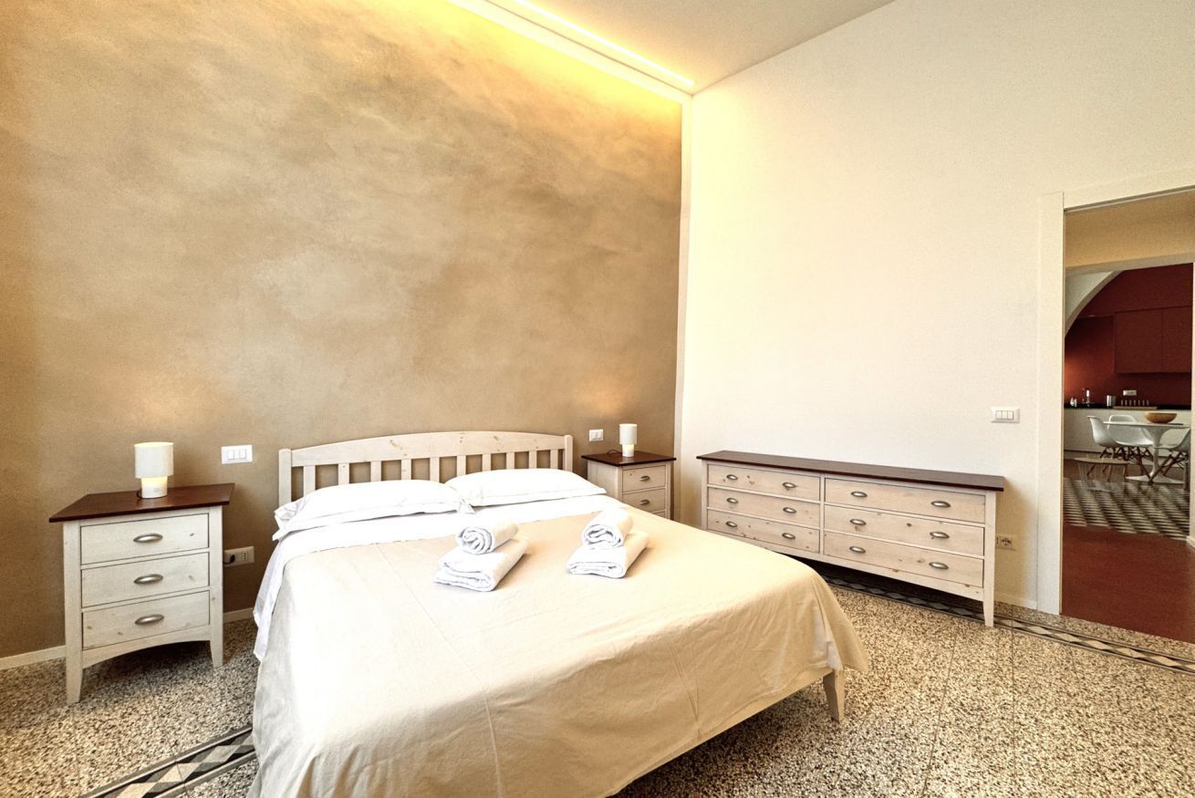 A neatly made bed with pillows and folded towels, a bedside table with a lamp, and a dresser with drawers.