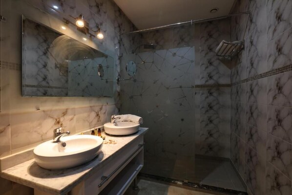 Un baño con tocador de mármol, dos lavamanos, un espejo grande y zona de ducha con mampara de cristal.