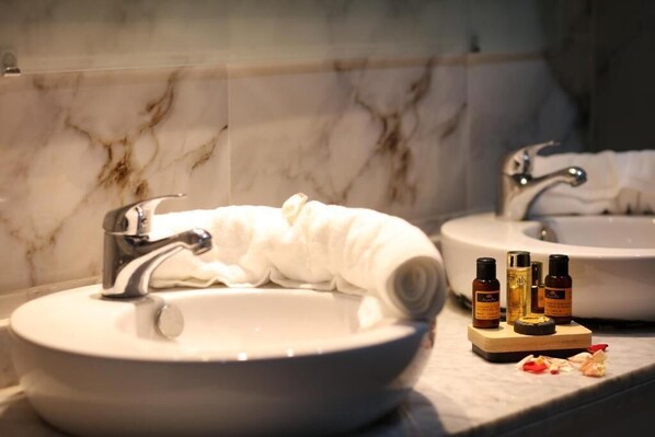 A bathroom with a marble sink, a towel, and three bottles of toiletries on the counter.