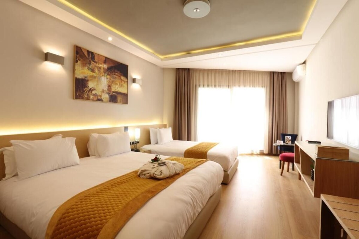 A hotel room with two beds, a desk, a chair, and a large window with curtains.