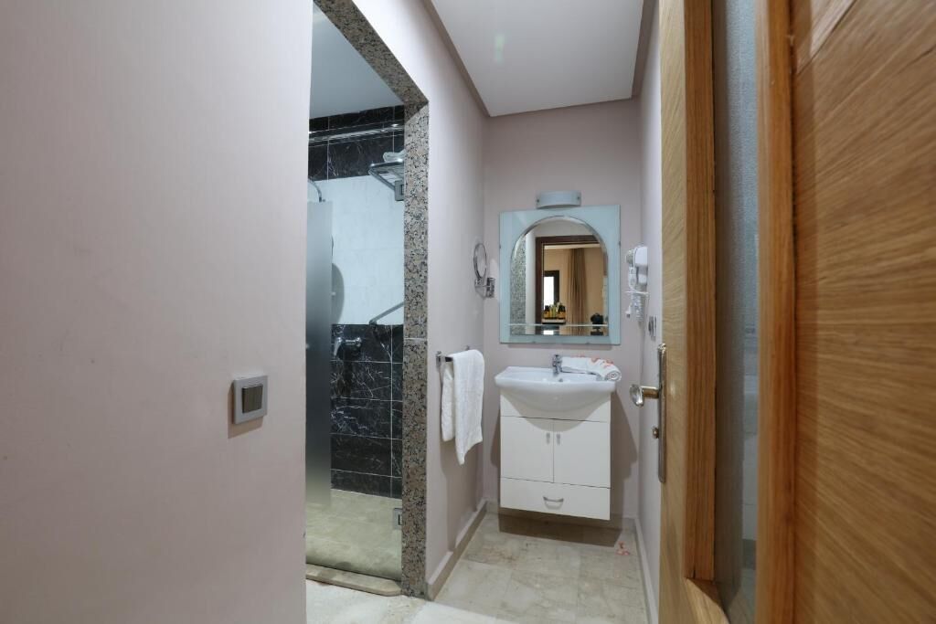 Un baño con ducha de mármol, lavabo con espejo y puerta de madera.