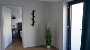 A modern hotel room with a wooden floor, a potted plant, and a wall-mounted coat rack. - Wine, space & well-being - your vacation apartment "Im Rosengarten - I" (Mommenheim)