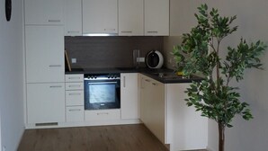 A modern kitchen with white cabinets, a built-in oven, and a small island with a microwave. - Wine, space & well-being - your vacation apartment "Im Rosengarten - I" (Mommenheim)