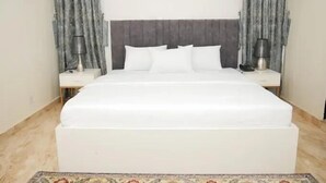 A neatly arranged bedroom with a large bed, two bedside tables, and a wall-mounted air conditioning unit. - Asher's Villa  (Abuja)